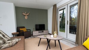 A living room with a sofa, a television, a small table, and a sliding glass door leading to an outdoor area. - Modern Villa Near Veluwe (Hoenderloo)