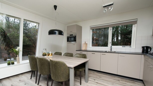 A modern kitchen with a dining table and chairs, a window, and a view of trees. - Modern Villa Near Veluwe (Hoenderloo)