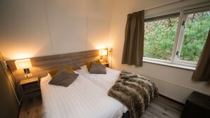 A bedroom with a large bed, two bedside tables, a window with curtains, and a view of trees outside. - Modern Villa Near Veluwe (Hoenderloo)