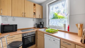 A compact kitchen with wooden cabinets, a microwave, an oven, a dishwasher, and a window with a view of greenery. - Ruhige Gartenwohnung in Dresden (Dresden)