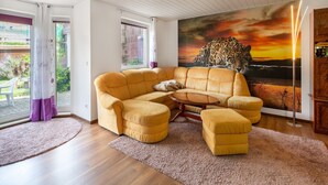 A living room with a yellow sofa, a matching ottoman, and a large painting of a leopard. - Ruhige Gartenwohnung in Dresden (Dresden)
