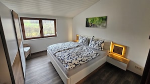 A bedroom with a large bed, a window, a bedside table, and a wall-mounted artwork. - Beautiful vacation apartment on the edge of the forest with three bedrooms. (Bad König)