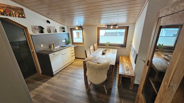 A compact kitchen with wooden flooring, a dining area with a table and chairs, and a window providing natural light. - Beautiful vacation apartment on the edge of the forest with three bedrooms. (Bad König)