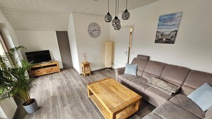 A modern living room with a brown sofa, wooden coffee table, and a TV on a wooden stand. - Beautiful vacation apartment on the edge of the forest with three bedrooms. (Bad König)