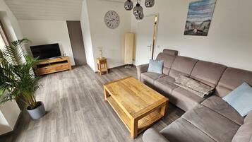 Ein modernes Wohnzimmer mit einem braunen Sofa, einem Holztisch und einem Fernseher auf einem Holzboden.