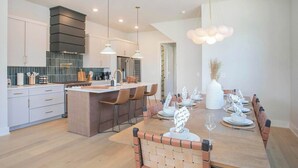 A modern kitchen with a central island, pendant lighting, and a dining area set for a meal. - 4 BDR Stay for 12 w/Rooftop Patio Firepit! Near DT (Nashville)