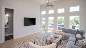 A spacious living room with a large flat-screen TV, a chandelier, a sofa, and a coffee table. - 4 BDR Stay for 12 w/Rooftop Patio Firepit! Near DT (Nashville)