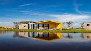 Een modern huis met een geel dak, grote ramen en een spiegeling in het water.