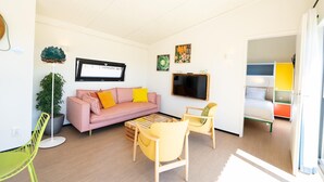 Een moderne woonkamer met een roze bank, gele fauteuils, een salontafel, een flatscreen televisie en een potplant.