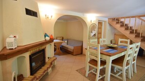 A cozy room with a fireplace, a dining table with chairs, a sofa, and a staircase.