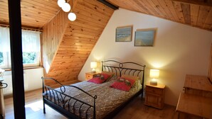 A bedroom with a sloped ceiling, a bed with two pillows, bedside lamps, and two framed pictures on the wall.