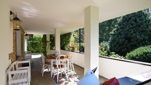 A covered patio with a table and chairs, a bird sculpture, and a view of greenery.