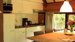 A kitchen with white cabinets, a wooden dining table, and a window with curtains. - Forest Hideaway with Fireplace (Herpen)