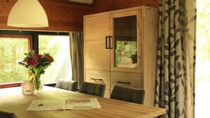 A wooden dining table with chairs, a vase of flowers, and a newspaper. - Forest Hideaway with Fireplace (Herpen)