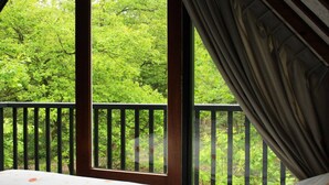 A room with a bed, a window with curtains, and a view of a forest. - Forest Hideaway with Fireplace (Herpen)