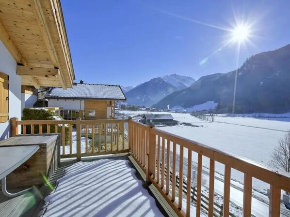 A wooden balcony with a view of a snowy landscape and mountains.