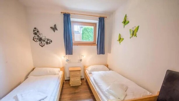 Acomodação pequena, com um quarto, duas camas de madeira, uma escrivaninha e uma cadeira.