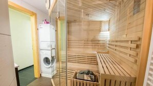Uma sala de sauna com um banco de madeira e uma máquina de lavar no quarto vizinho.