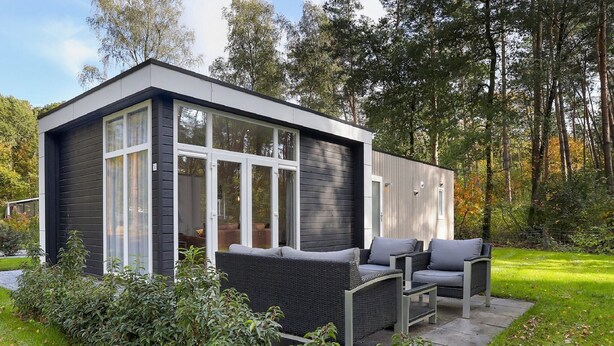 Une maison moderne dotée de grandes fenêtres, d’un patio avec mobilier d’extérieur et d’un jardin.