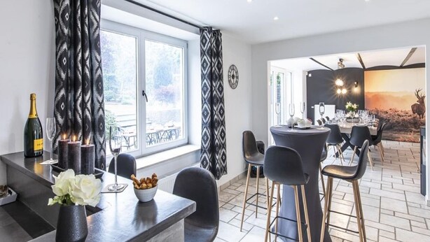 A dining area with a table set for six, a bottle of champagne, and candles on the windowsill. - Holiday Home in Manhay near Ski Area (Manhay)