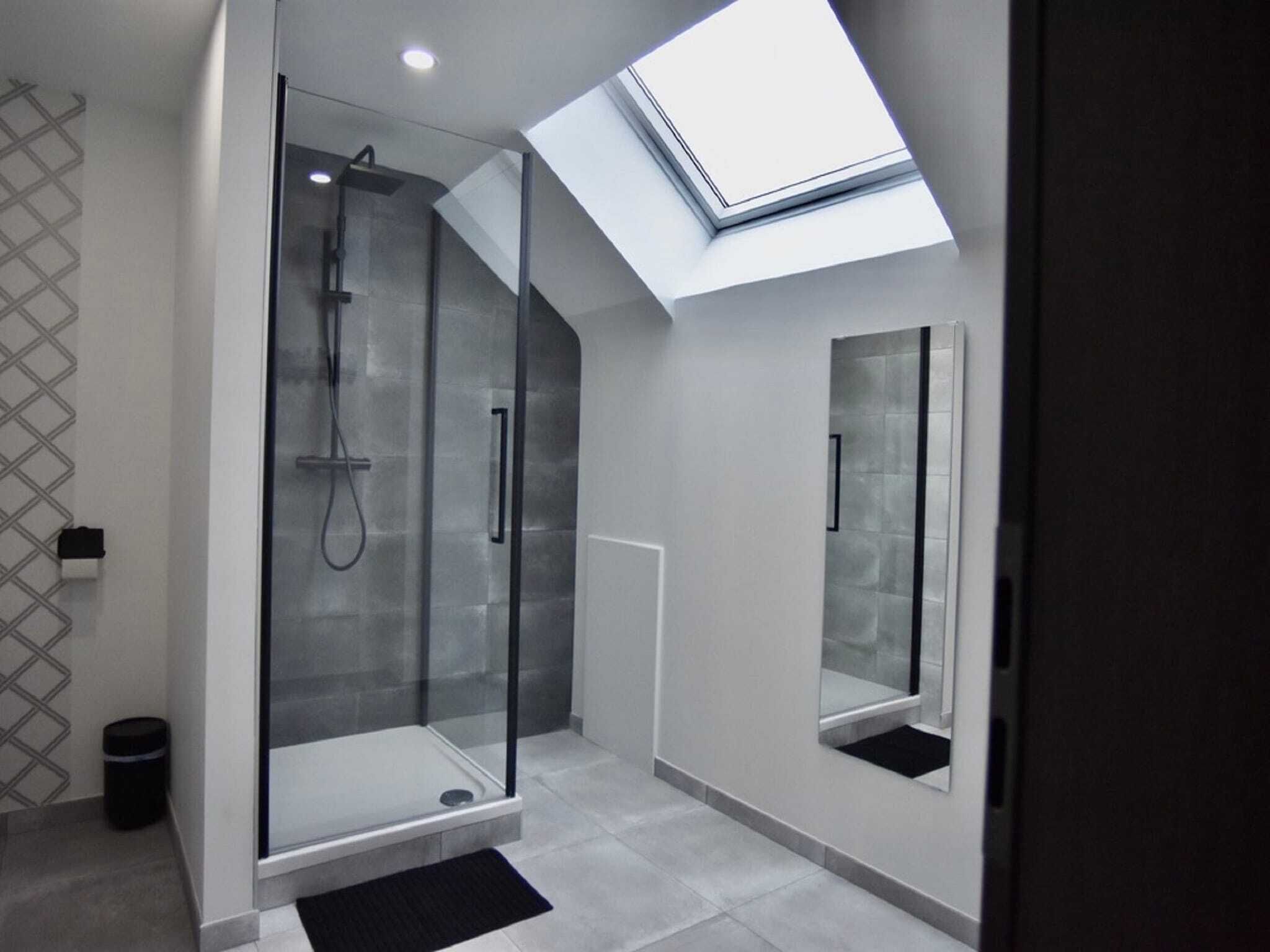 Un baño moderno con ducha cubierta por vidrio, tragaluz y un espejo grande.