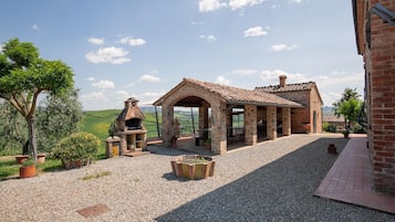 Un espace extérieur rustique avec un barbecue en pierre, des sièges et une vue sur la campagne.