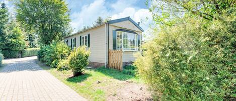 Une maison mobile de plain-pied dotée d’une grande fenêtre, entourée de verdure et donnant sur une allée pavée.