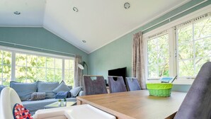A dining area with a wooden table, chairs, and a high chair. There is a television on a stand and a window with curtains. - Chalet in Stegeren near Hiking Trails (Stegeren)