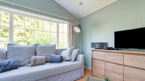 A living room with a grey sofa, a wooden cabinet, a flat-screen TV, and two potted plants. - Chalet in Stegeren near Hiking Trails (Stegeren)