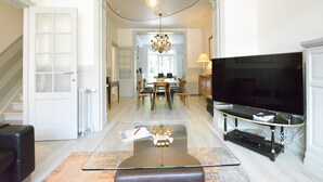 Een moderne woonkamer met een glazen salontafel, een televisie op een meubel en een kroonluchter.