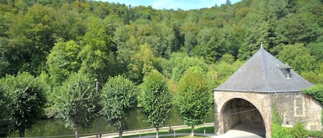 A stone bridge with a pointed roof, surrounded by lush green forest and a body of water.