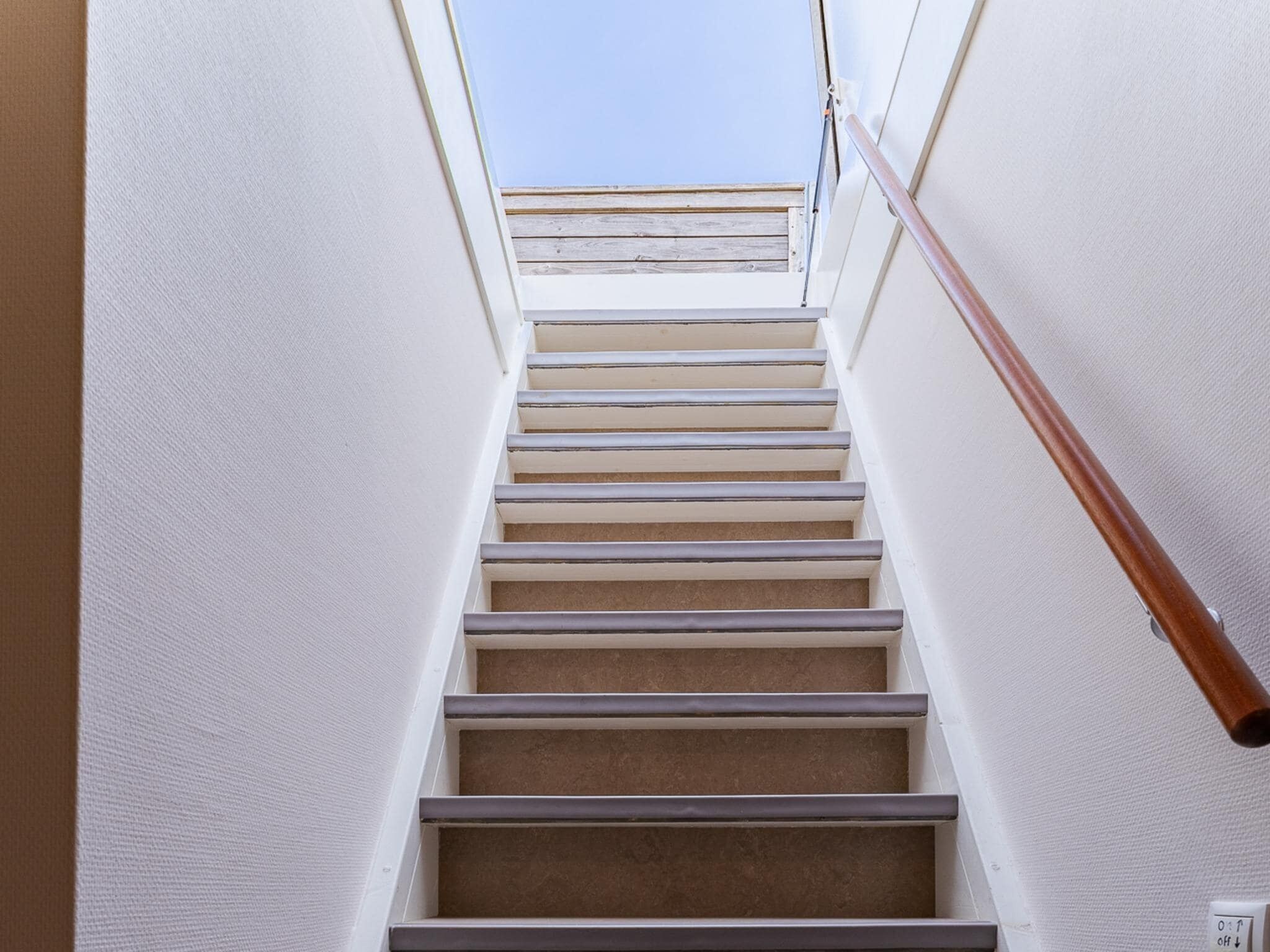 Una escalera con barandilla de madera y tragaluz en la parte superior.