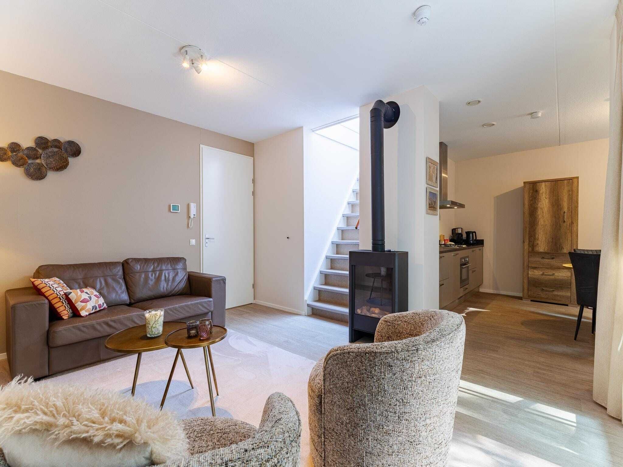 Una sala moderna con un sofá, una mesita redonda y un sillón mullido. Una escalera conduce a una zona de cocina con una estufa.