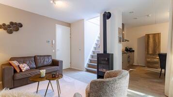 Una sala moderna con un sofá, una mesita redonda y un sillón mullido. Una escalera conduce a una zona de cocina con una estufa.