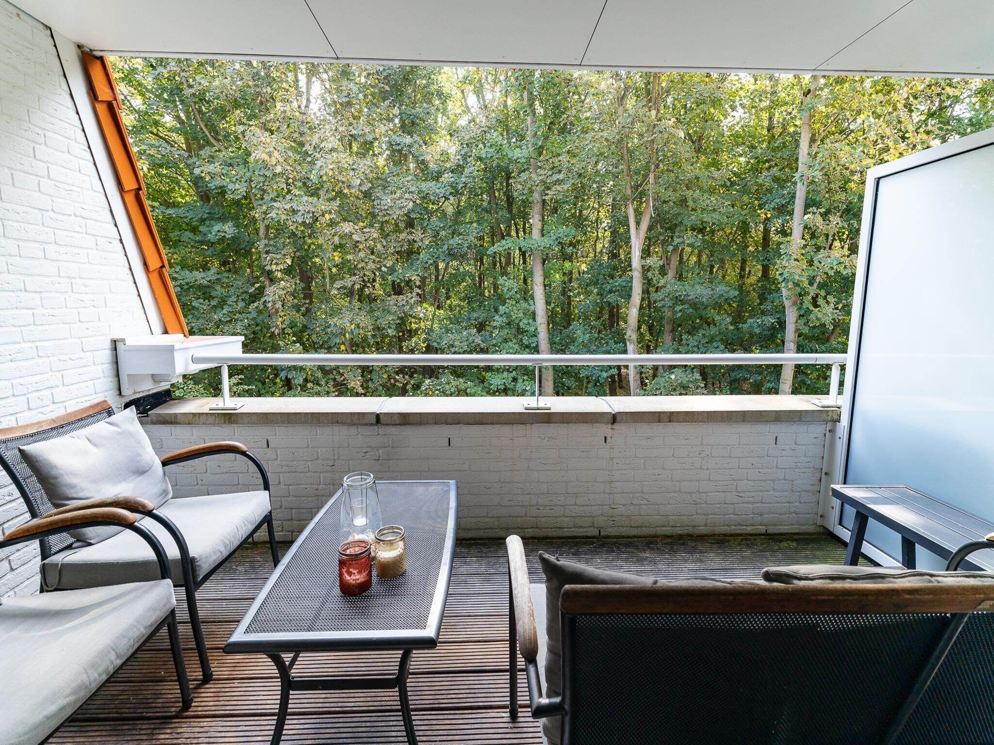 A balcony with a white brick wall, a sofa, a table with two glass jars, and a view of a dense green forest.