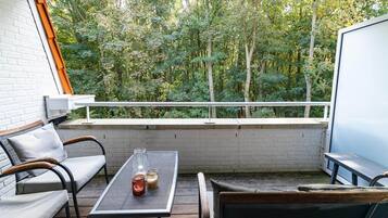 A balcony with a white brick wall, a sofa, a table with two glass jars, and a view of a dense green forest.