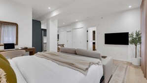 Una habitación de hotel moderna con una cama grande, un escritorio con una computadora portátil, un televisor de pantalla plana y una planta en maceta.