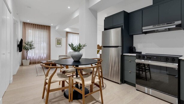 Una cocina moderna con armarios oscuros, un refrigerador de acero inoxidable y un horno. Hay un comedor con una mesa redonda y sillas.