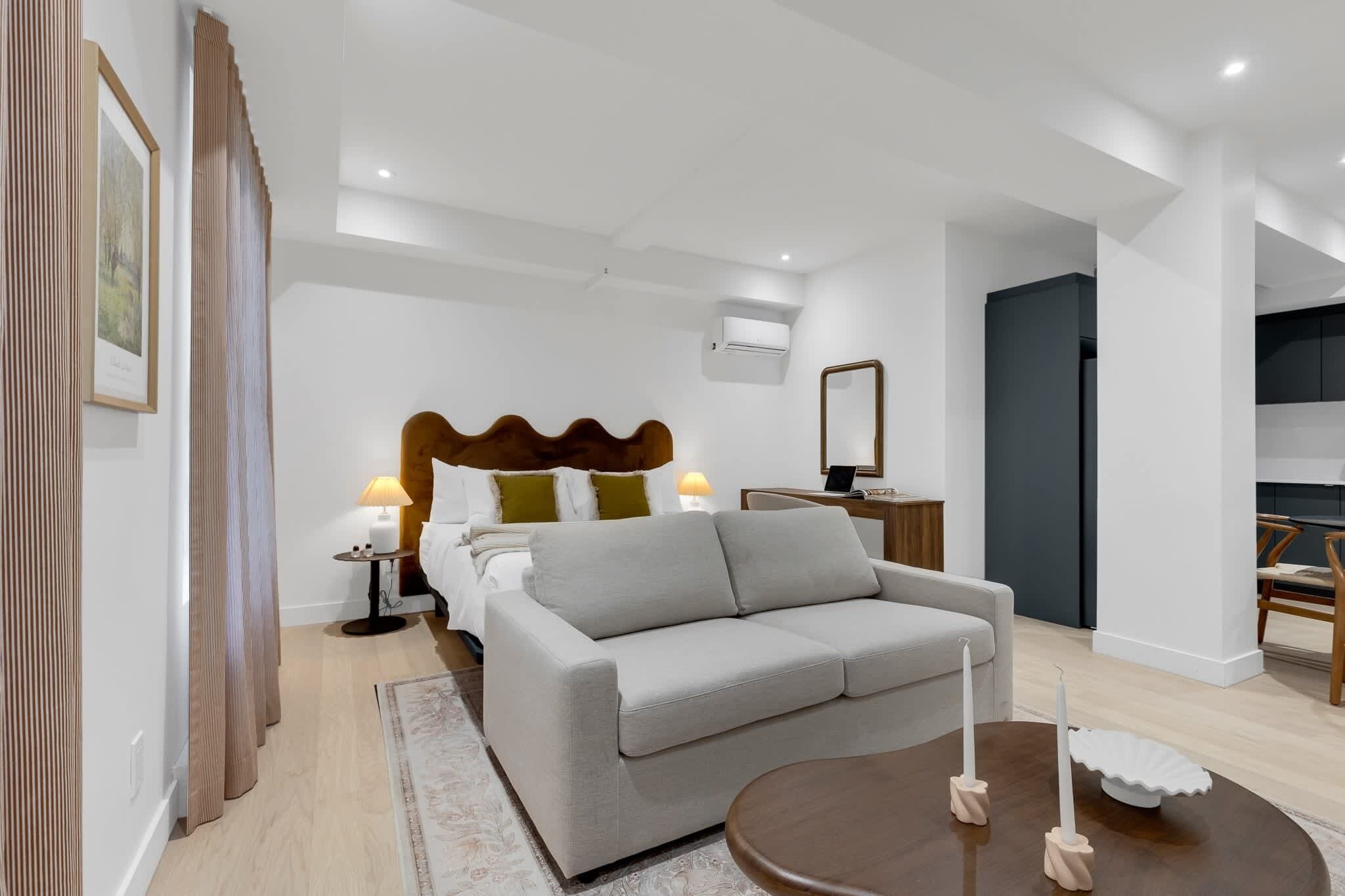 A modern hotel room with a bed, a sofa, a coffee table, and a dining area.