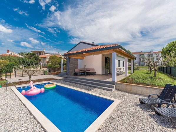 A swimming pool with a covered patio area, surrounded by a garden and residential buildings. - Villa in Novigrad with Private Pool and Beach (Novigrad)