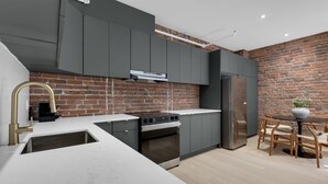 A modern kitchen with grey cabinets, a brick wall, a stainless steel oven, and a dining area with wooden chairs and a table. - Mercer-2BDR 2BA Old Montreal- Free parking (Montréal)