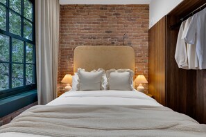 A bedroom with a brick wall, a large window, a bed with white bedding, and two bedside lamps. - Mercer-2BDR 2BA Old Montreal- Free parking (Montréal)