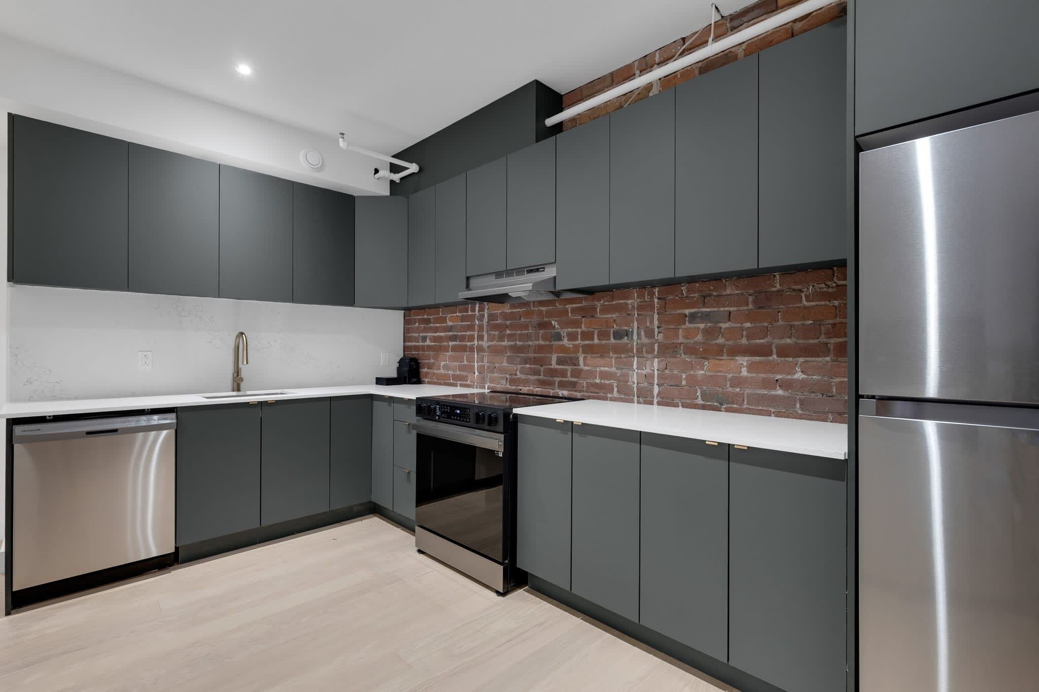 A modern kitchen with grey cabinets, a brick wall backsplash, stainless steel appliances, and a dishwasher.