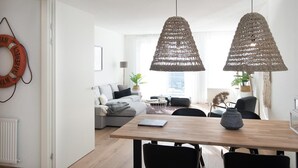 Una sala de estar moderna con una mesa de comedor de madera, sillas negras, un sofá gris y un ventanal grande.