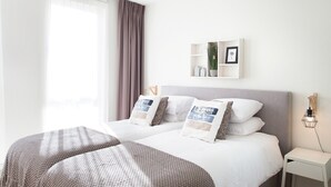 Un dormitorio moderno con una cama grande, una mesita de noche, un estante en la pared y una ventana con cortinas.