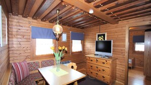 A cozy cabin interior with a wooden ceiling, a dining table with a vase of flowers, a sofa, a TV, and a dresser. - Apartment in Fresach near Ski Slopes (Fresach)