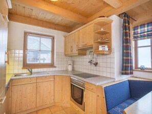 Eine kleine Küche mit Holzschränken, einem Einbauofen, einem Spülbecken und einem Fenster mit Jalousien.