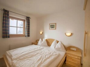 Un dormitorio con cama, una ventana con cortinas, dos lámparas de noche, un cuadro en la pared y una mesita de noche de madera.