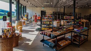 Ein geräumiger Supermarkt mit breiten Gängen, einer vielfältigen Auswahl an Produkten auf Regalen und einem rustikalen Holzbottich.