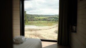Ein Zimmer mit großem Fenster und Blick auf eine ländliche Landschaft, darunter Felder und ein Feldweg.